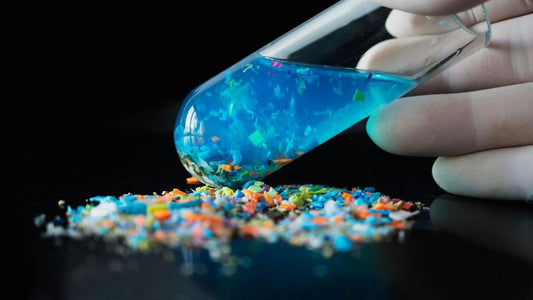 Hånd med reagensglas over farverige mikroplastpartikler — illustration af mikroplastforurening og forskningen i plastpartiklers påvirkning af biologisk aldring